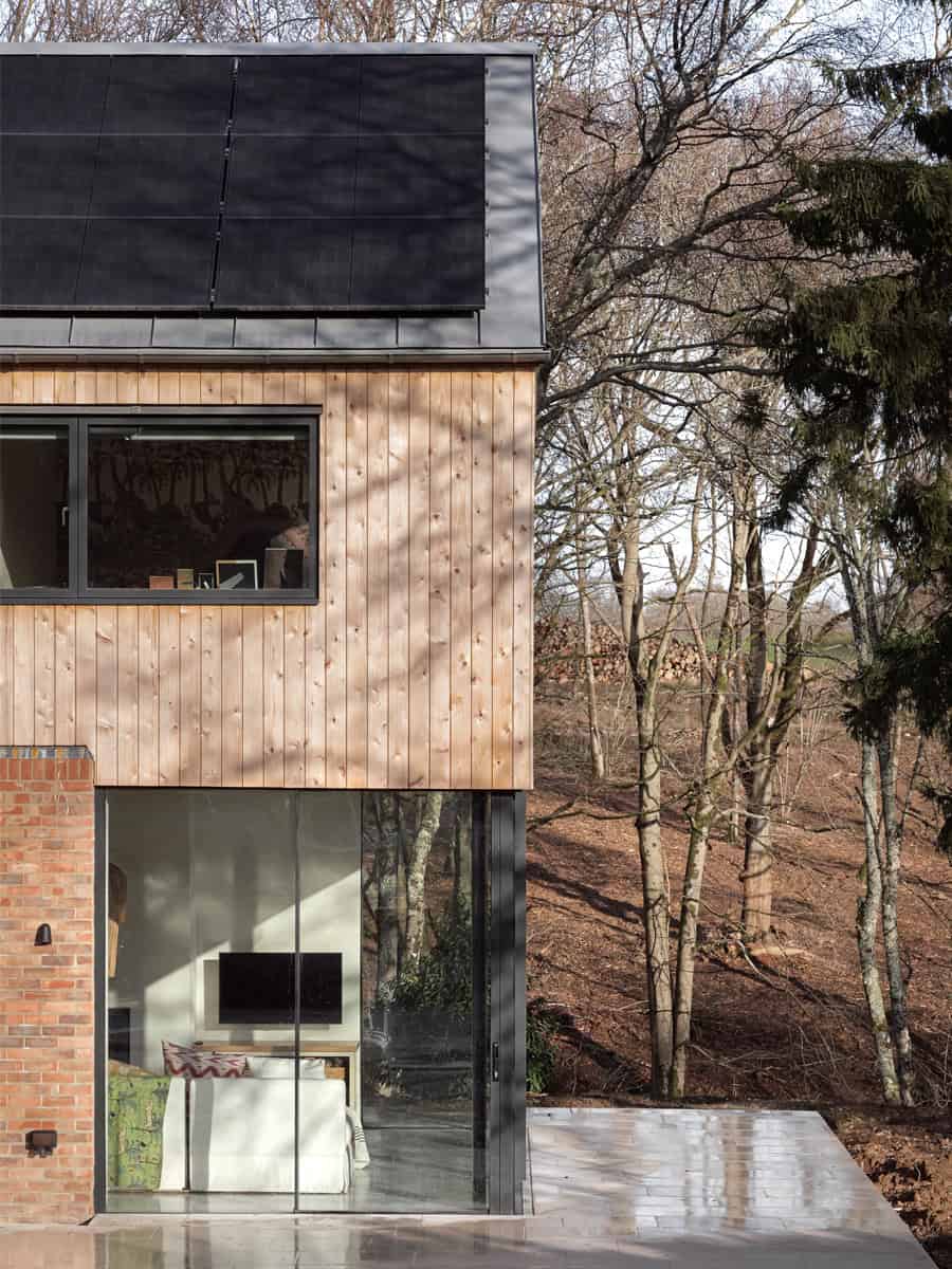 Hazelbridge Cottage exterior detail with timber cladding, brick, solar panels, and woodland setting